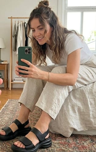 Reviewer sitting on a bed, wearing the black Modesty platform sandals with casual pants.