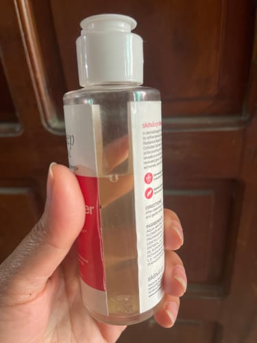 A reviewer holds a half-full clear bottle of Daily Glow Glycolic Toner in their hand.