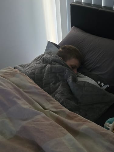 Customer shows a person sleeping soundly under the grey, quilted Weighted Blanket II.