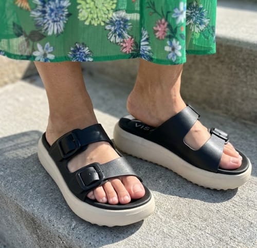 Reviewer wearing the black Soothe sandals with a thick, off-white platform sole while standing on stone steps.