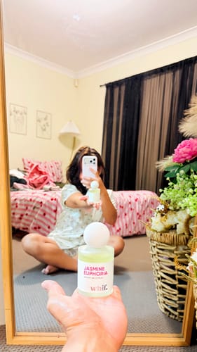 Reviewer holding a bottle of Jasmine Euphoria perfume in front of a mirror, with their reflection visible in the background.