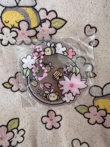 Close-up of the bee and blossom shaker charm resting on the reviewer's Bees & Blossoms Journal Buddy.