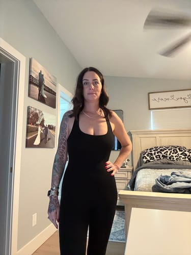 Reviewer posing in a bedroom wearing the black NW Sculpt Racerback Jumpsuit.