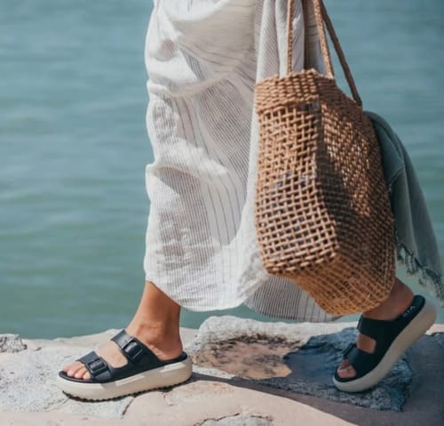 Customer walking in black Soothe sandals with a thick white platform sole outdoors.