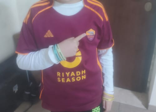 Un cliente indossa la Maglia Roma Home e ne indica lo stemma con il dito.