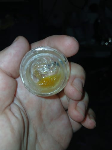 Customer holding a small open jar of the golden, waxy THCa Badder in their palm.