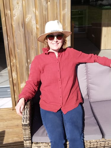 Cliente portant la blouse Marthe terre de sienne avec un jean, assise en extérieur sur un canapé.