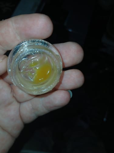 Close-up of a reviewer's hand holding an open jar of golden Live Hash Rosin.