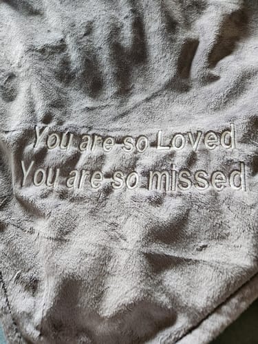 Close-up of a customer's T-Shirt Quilt showing the custom embroidery "You are so Loved You are so missed" on the soft grey backing.