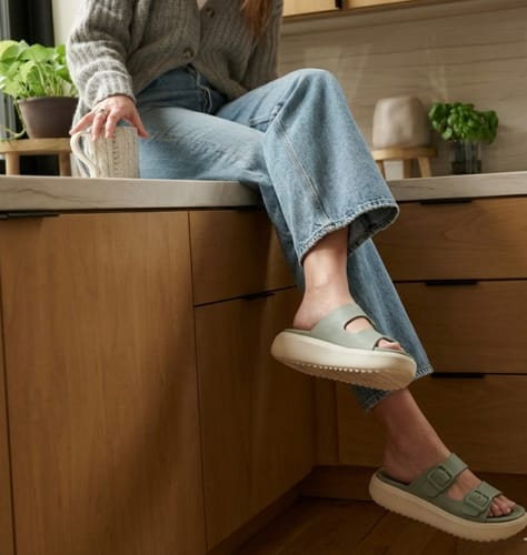 Reviewer wearing light green Soothe platform sandals while relaxing on a kitchen counter.