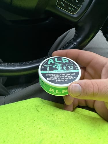 Customer holding a light green can of ALP Refreshing Chill Nicotine Pouches in their car.