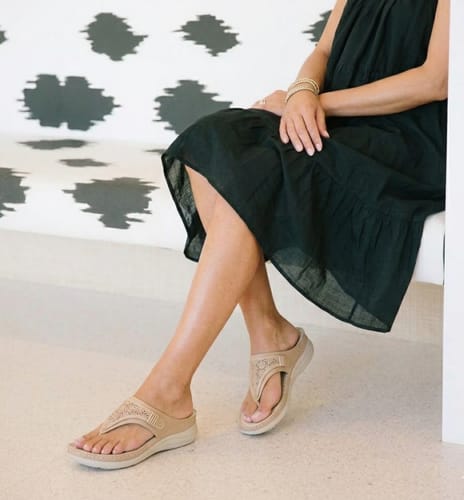 Customer sitting on a bench, wearing the beige Grace wedge sandals with a black dress.