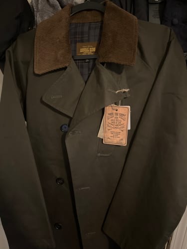 Close-up of a customer's WWII Dispatch Rider’s Coat on a hanger, showing the brown corduroy collar and plaid lining.