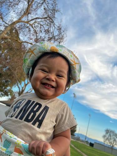 Customer's smiling baby wearing the patterned Sailor baby cotton hat outdoors.