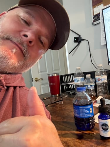 Reviewer with a thumbs-up shows a bottle of Meraki Blu Methylene Blue and the product mixed in a water bottle on a desk.