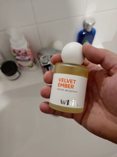 Customer's hand holding a small bottle of Velvet Ember perfume in a bathroom.