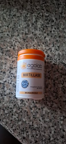 Recensore mostra la confezione bianca di Mirtillase con tappo arancione su un bancone.