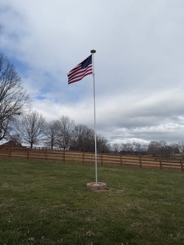 Reviewer's Ultra Heavy Duty American Flag flying on a flagpole in a grassy field under a cloudy sky.