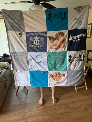 Reviewer holds up their large, multi-colored Premium T-Shirt Quilt, displaying various shirt designs from their collection.