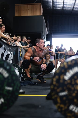 Reviewer crouching mid-workout, wearing black FROG GRIPS® ELITE HD fingerless grips in a gym.