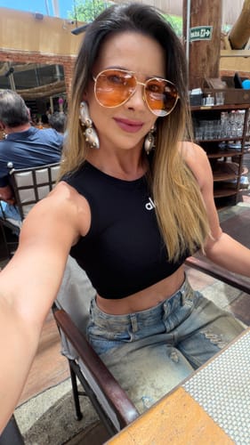 Cliente em uma selfie usando os Óculos Savona com lentes laranjas e fina armação dourada.