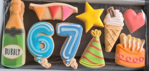 Customer's Birthday Balloon Deluxe Biscuit Box with colorful iced biscuits, showing the number 67, a bubbly bottle, and a cake.