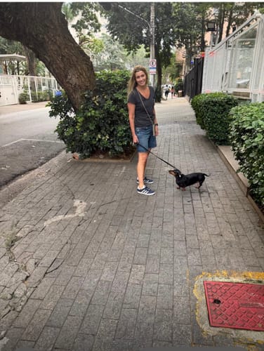 Avaliadora passeando com seu cão, usando a case Odara com alça na cor areia de forma transversal.