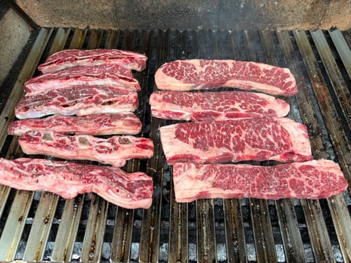 Reseñador cocinando tiras crudas de Asado de Tira en una parrilla caliente.