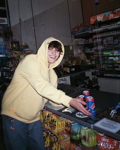 Reviewer smiling in a store while wearing the yellow VISIONZ SWEATS hoodie.