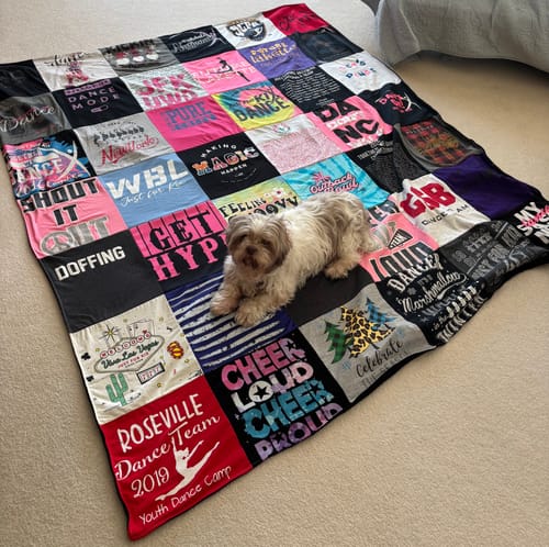 Customer's large Premium T Shirt Quilt made of colorful dance shirts, with their small dog lying on it.
