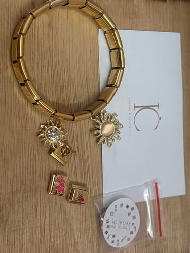 Reseña de cliente de la pulsera italiana dorada sobre una mesa, junto a varios charms de sol y eslabones.