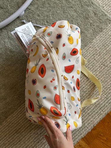 Customer holding the Clementine portable booster chair inside its vibrant, fruit-patterned carry bag.