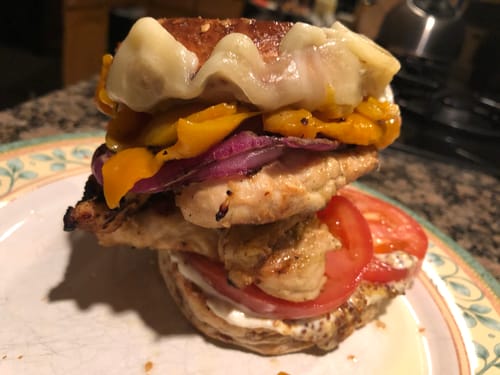 Close-up of a reviewer's tall sandwich made with Halal Chicken Leg & Thigh, layered with cheese and vegetables.