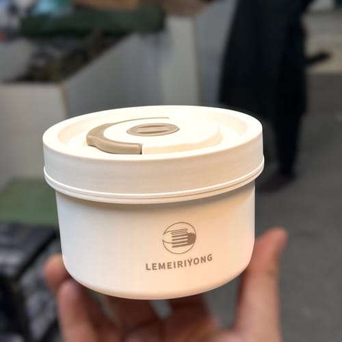 Customer holding the white, round stainless steel lunch box in their hand against a blurred background.