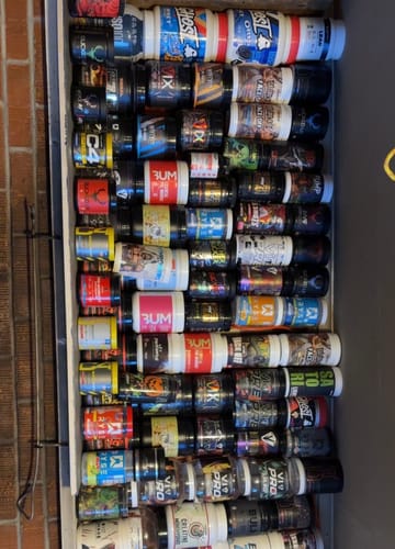 Reviewer's large collection of pre-workout supplement tubs, with several V1X PRODIGY containers visible.