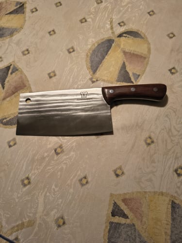 Rezensent zeigt das schwere chinesische Hackmesser mit geschmiedeter Klinge und Holzgriff auf einer Tischdecke.