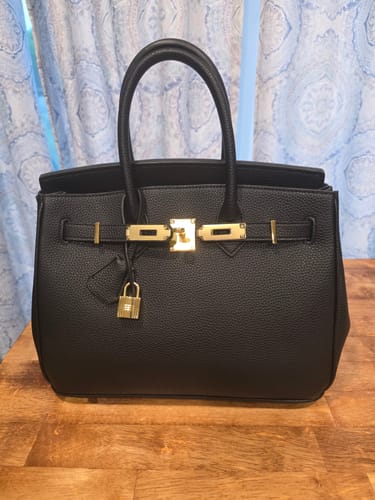 Customer's black Warkin Bag with gold lock hardware, sitting on a wooden table.