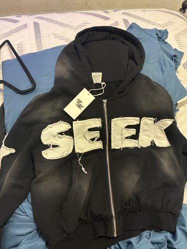Customer's black SEEK ZIPUP laid out, showing the large, distressed white lettering across the chest.