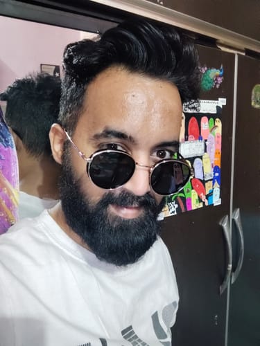 Reviewer smiling while wearing the stylish Captain gold and black round sunglasses indoors.