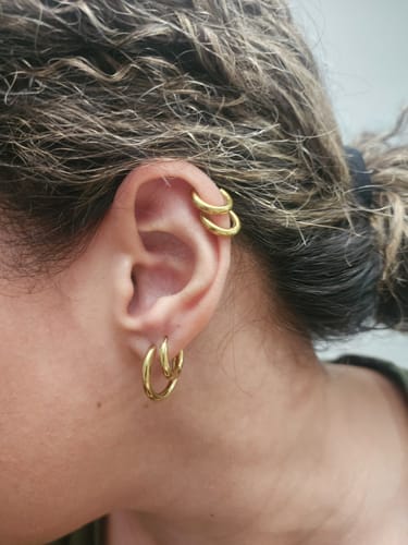 A close-up of a customer's ear showing the Gold Trio Mini Hoop Set worn on the lobe and cartilage.