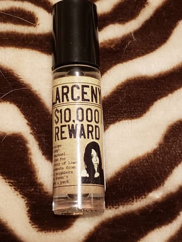 Customer's Larceny perfume rollerball with a wanted poster label lying on a zebra-print fabric.