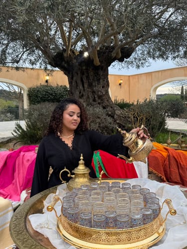 Reviewer wearing the black Kaftan Saida with lace details while pouring tea at an outdoor event.