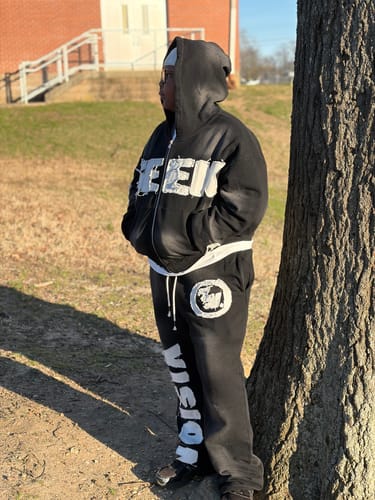 Customer standing outdoors wearing the black SEEK VISIONZ SET, a matching hoodie and pants.