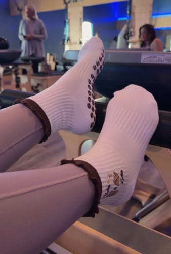 Customer wearing white Pilates socks with grip soles and ruffled cuffs in a Pilates studio.