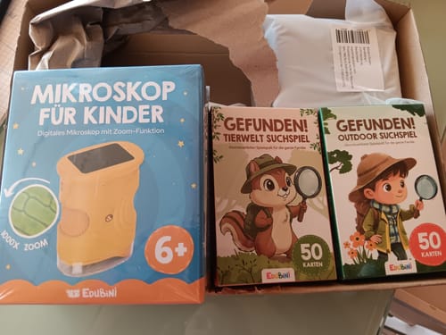 Kunde zeigt die Schachtel des „Gefunden! Tierwelt Suchspiel“ in einer Lieferbox mit anderen Lernspielen.