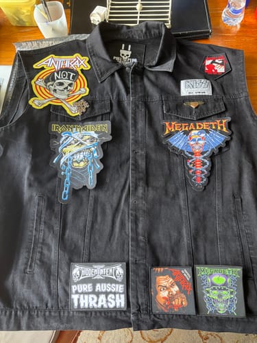 Reviewer's black 'The Left Hand Black - Vest' laid flat with several colorful band patches applied to the front.