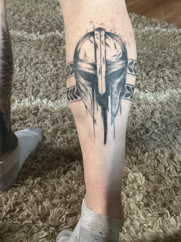Customer shows their detailed Mandalorian helmet tattoo on their calf after using the numbing cream.