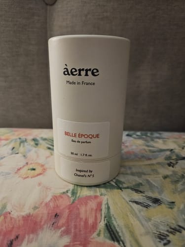 Customer's white cylindrical packaging for Belle Époque perfume shown on a colorful floral surface.