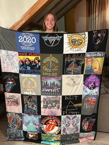 Reviewer holding up a large Premium T Shirt Quilt made from various classic rock band t-shirts.