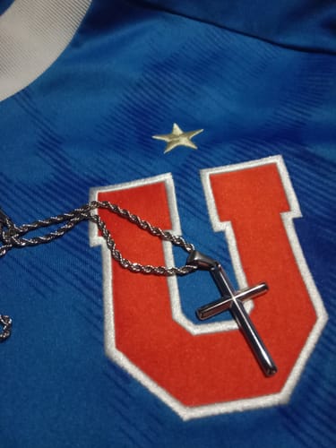 Cliente muestra el colgante Crucifijo y la cadena de cuerda sobre una camiseta deportiva azul.